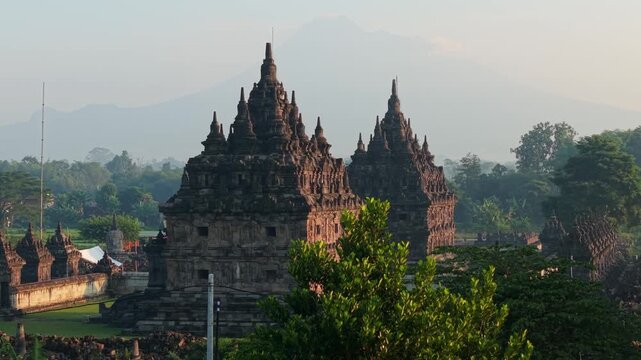 Aerial view of Plaosan Lor Temple featuring ancient stone structures surrounded by lush green foliage and hazy mountains in Kecamatan Prambanan, Jawa Tengah, Indonesia.