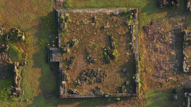 Aerial view of Plaosan Kidul Temple ruins with ancient stone foundations and scattered blocks on green grass in Kecamatan Prambanan, Jawa Tengah, Indonesia.