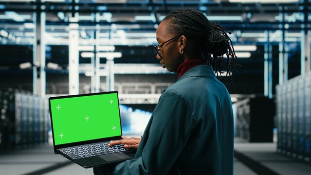 Green screen laptop in data center and AR tech used by technician to visualize and debug system errors, Server farm expert uses mockup notebook to run diagnostics on wireframe mesh gear, camera B.