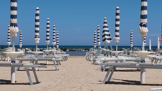 Sunny sandy beach ready for summer season, with umbrellas closed and no people. Italy, Senigallia