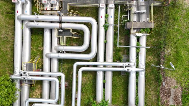 Aerial view of interconnected industrial pipes with green grass and walkways visible, showcasing the complex layout of a facility's piping system in an industrial setting