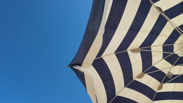 Abstract view of striped beach umbrella moved by wind during a sunny day at Senigallia beach. Marche, Italy.