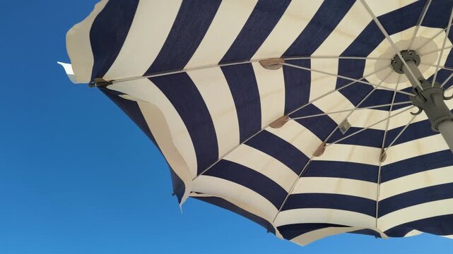 Abstract view of striped beach umbrella moved by wind during a sunny day at Senigallia beach. Marche, Italy.