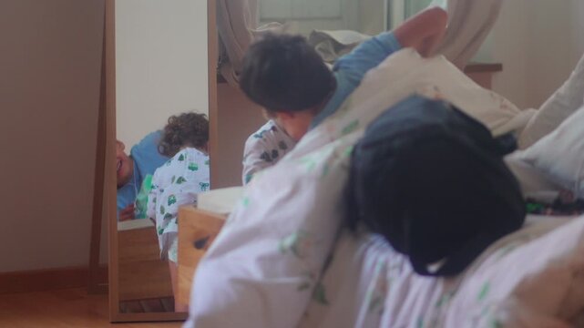 Toddler investigating moving duvet on bed before older sibling appears during playful family hide and seek game indoors at home