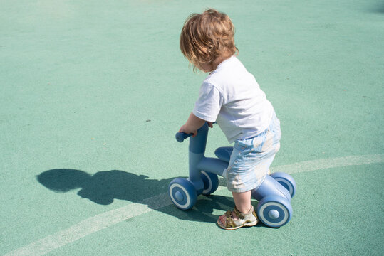Tiny child straddling blue balance bike on outdoor sports court