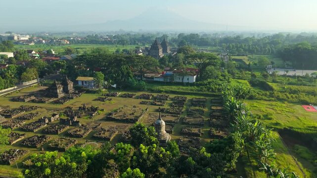 Aerial view of Plaosan Lor Temple featuring ancient stone stupas and ruins surrounded by lush green vegetation and fields in Kecamatan Prambanan, Jawa Tengah, Indonesia.
