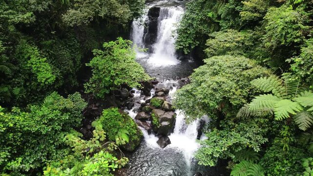Aerial view of Ambyar waterfall cascading over rocks surrounded by dense green tropical jungle and lush foliage Purwokerto, Central Java, Indonesia.