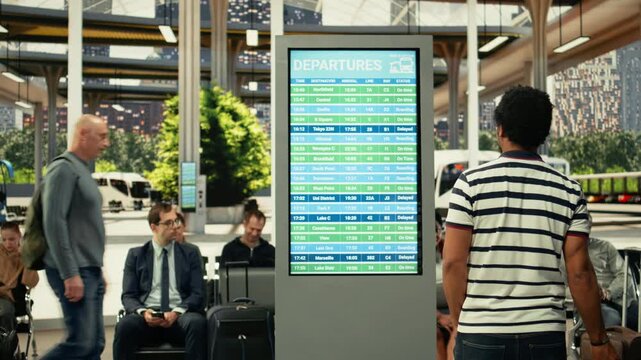 African american traveler checking timetable on departure board in bus terminal, waiting for long-haul interstate coach. Diverse commuters in transit hub for life in motion concept.