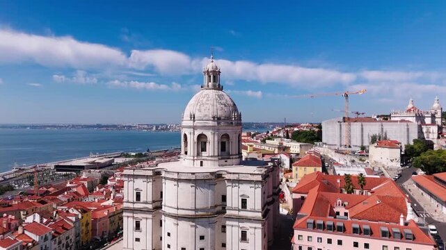 Aerial establishing shot of the National Pantheon rising above blooming jacaranda trees in Campo de Santa Clara, Lisbon, Portugal.
