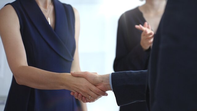 Business executives shaking hands during a successful corporate meeting, finalizing an important deal while a colleague claps in approval, symbolizing strong teamwork and growing success
