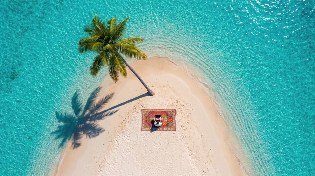 Top view of man freelancer on rug under palm tree on tropical beach island working on laptop. Drone shot of digital nomad remote office. Freelance work at computer. Small business with copy-space.