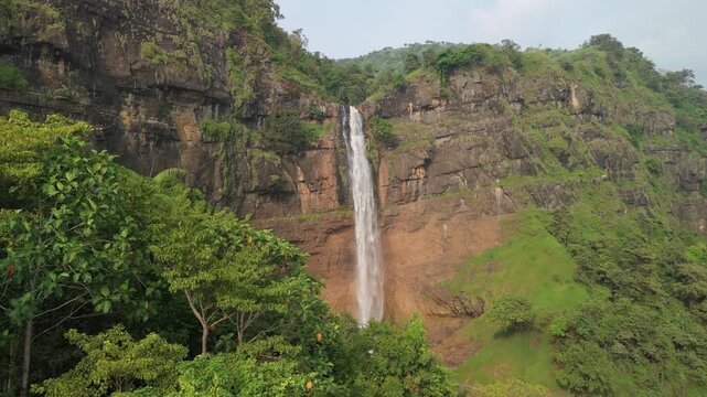 Aerial view of Cikanteh Waterfall cascading down a steep rocky cliff surrounded by dense tropical forest and green trees in Sukabumi, West Java, Indonesia.