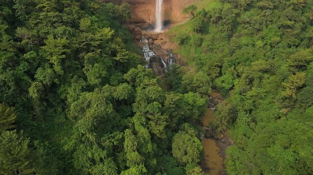 Aerial view of Cikanteh Waterfall surrounded by lush tropical forest and a winding brown river in Sukabumi, West Java, Indonesia.