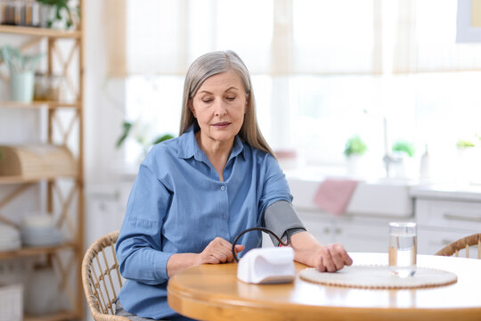 Senior woman measuring blood pressure at wooden table indoors