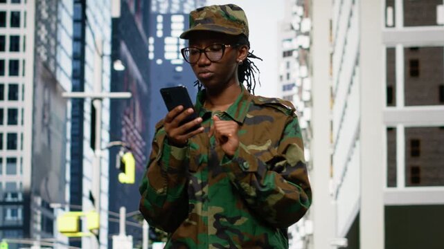 Army soldier examines smartphone map app and walking on city street, metropolitan area downtown. Black military officer using phone navigation to check tactical route coordinates, city center.