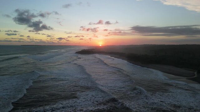 Aerial view of the sunset over the rolling waves and coastline of Ujung Genteng Beach in Kecamatan Ciracap, Jawa Barat, Indonesia.