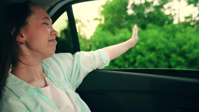 Beautiful student goes on vacation, holidays. Teenage girl traveling by car. Young passenger catches wind with hands from car window. Family trip. Family vacation. People traveling. Girl smile, travel