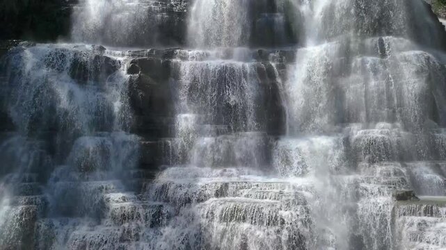 Aerial view of Cigangsa Waterfall with water cascading over dark tiered rock formations and mist rising in Sukabumi, West Java, Indonesia.