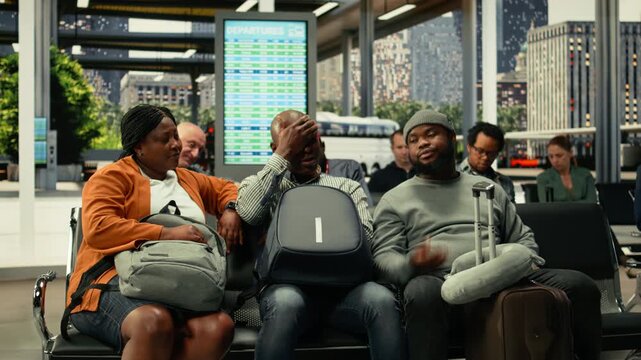 Worried tourists waiting in crowded coach station after cancelled long-haul departure. Fatigued passengers sitting in the waiting area with carry-on bags, watching departure board updates and delays.