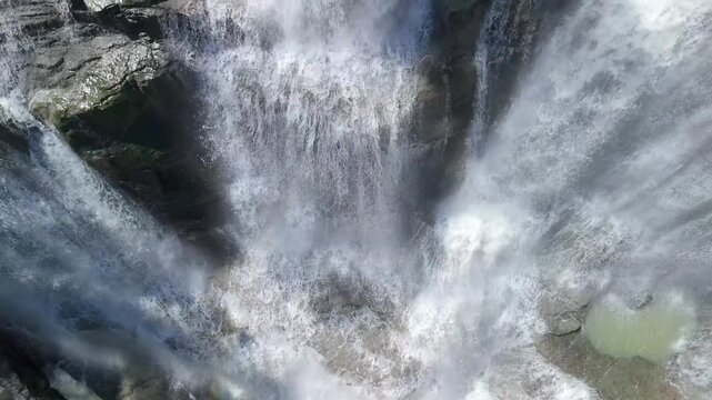Aerial view of Cigangsa Waterfall with powerful cascading water over dark rocky cliffs and mist in Sukabumi, West Java, Indonesia.