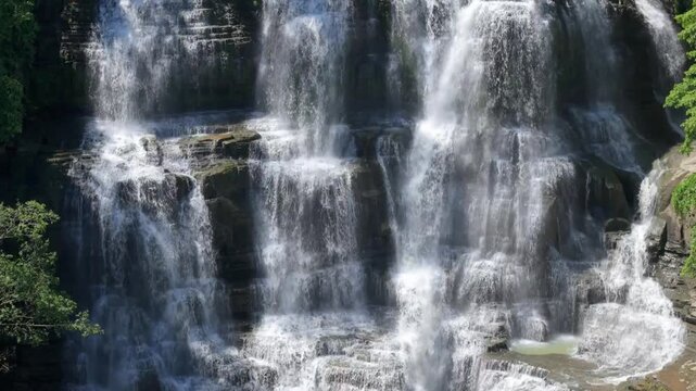 Aerial view of Cigangsa Waterfall cascading over dark rocky tiers surrounded by lush green foliage in Sukabumi, West Java, Indonesia.