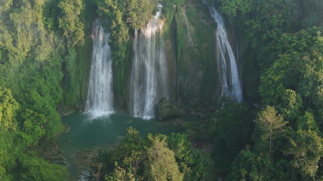 Aerial view of the three cascades of Cikaso Waterfall flowing into a turquoise pool surrounded by lush tropical forest in Sukabumi, West Java, Indonesia.