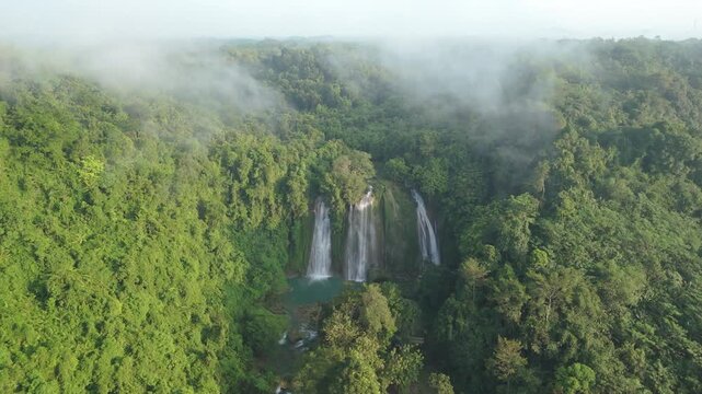 Aerial view of Cikaso Waterfall cascading into a turquoise pool surrounded by dense tropical jungle and morning mist in Sukabumi, West Java, Indonesia.