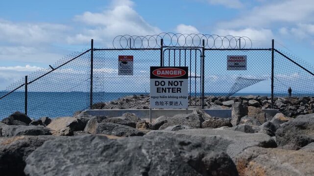 Security wire fence blocking access to a rocky groyne or breakwater structure at Werribee South, Victoria. A trilingual warning sign reads "DANGER DO NOT ENTER" in English, Vietnamese, and Chinese