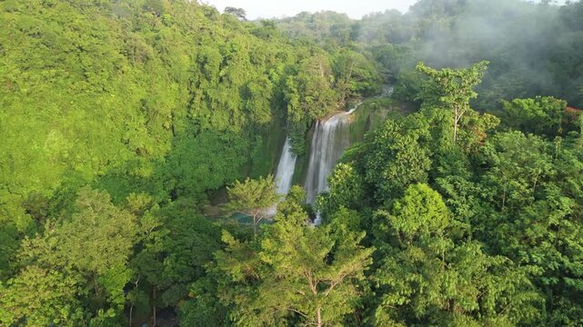 Aerial view of Cikaso Waterfall cascading through dense tropical rainforest with morning mist and lush green trees in Sukabumi, West Java, Indonesia.