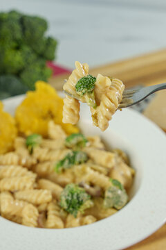 close up of a fork with pasta and vegetables with fried platain