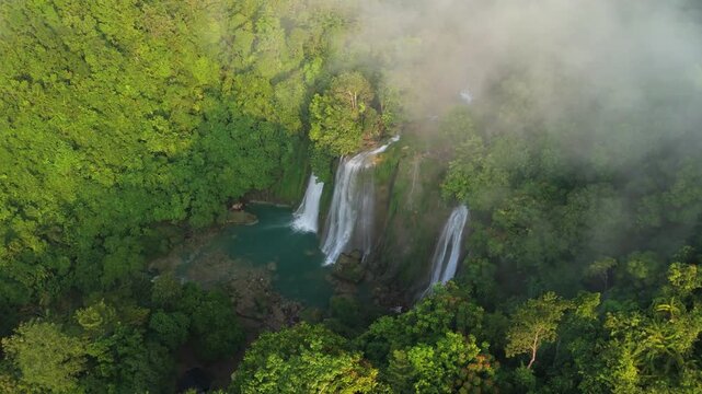 Aerial view of Cikaso Waterfall cascading into a turquoise pool surrounded by lush tropical jungle and morning mist in Sukabumi, West Java, Indonesia.