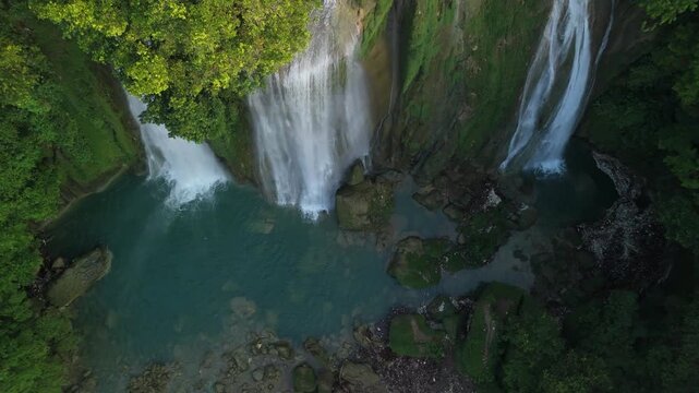Aerial view of Cikaso Waterfall with powerful cascades falling into a turquoise pool surrounded by lush tropical greenery in Sukabumi, West Java, Indonesia.