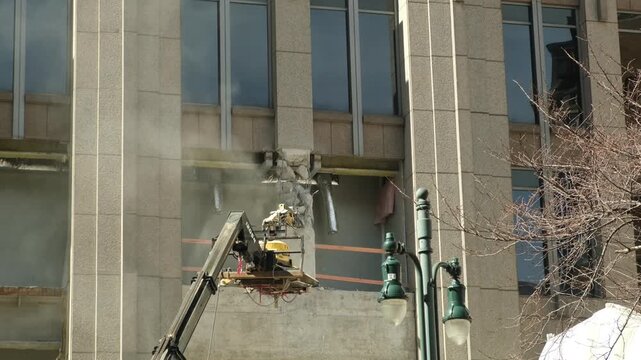 construction workers remove a section of a building in a city during the day