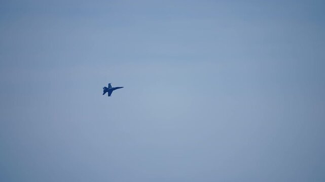 Slow motion of a twin engine military fighter jet performing a sharp banking turn against a hazy grey blue sky