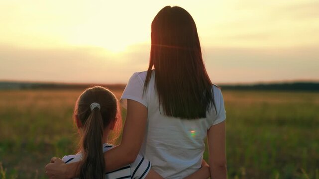 Mother, child girl hug on sunny day. Happy daughter hugs mother outside. Girl hugs mama in sun park. Happy family on walk in field, looking to future. Carefree childhood mother child. Unity parent kid