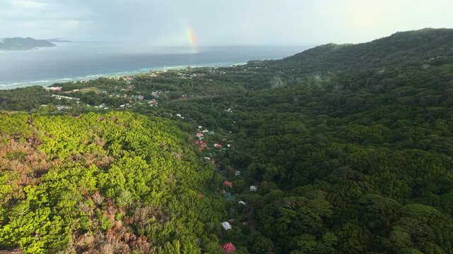 Aerial view of a rainbow over the lush green valley and coastline of Anse Reunion, La Digue, Seychelles.