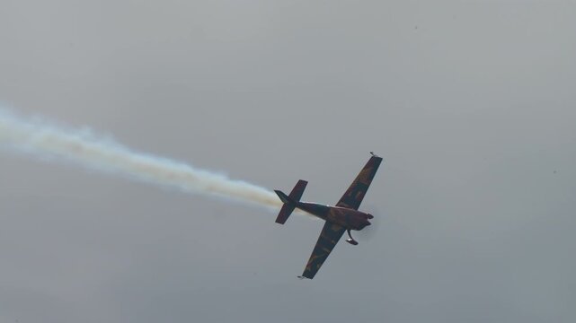 Light sports airplane performing an aerobatic maneuver leaving a white smoke trail in a hazy sky