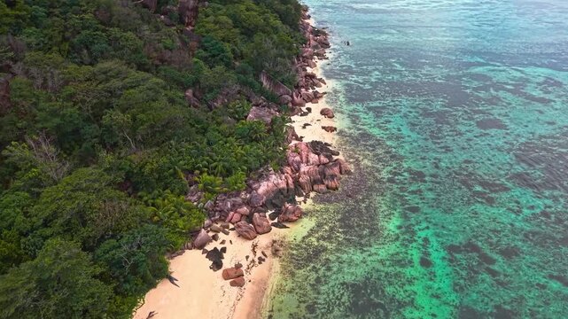 Aerial view of Anse Reunion beach featuring turquoise coral reefs, white sand, and granite rocks bordered by lush tropical forest in Anse Reunion, La Digue, Seychelles.