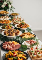 Fototapeta premium An elegant spread of diverse culinary delights arranged on a long banquet table with tiered platters, fresh greenery, and warm ambient lighting, platter, catering, snack