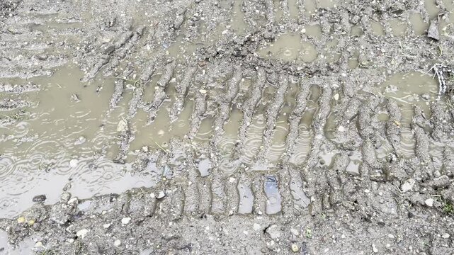 treads imprinted in the mud from heavy machinery with puddles of water in the rain