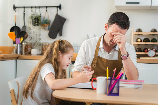 Exhausted father helping daughter with homework at home, Stressed dad struggling to assist daughter with schoolwork, Tired parent supporting primary school student with study