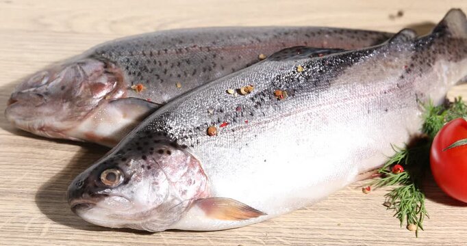 Sprinkling spices onto raw trout fish at wooden table table, closeup
