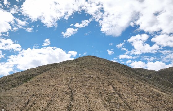 Vista contrapicada de un cerro &aacute;rido bajo un cielo azul brillante con nubes blancas