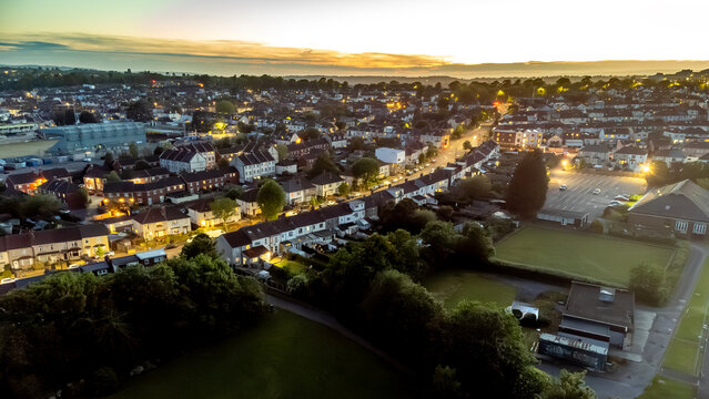 An aerial view of a neighborhood at dusk, with streetlights illuminating the houses and streets.