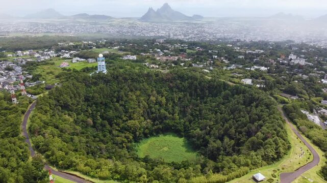 Drone footage over Trou aux Cerfs volcano in Mauritius, revealing its lush crater with the mountains and the town of Curepipe stretching beyond.