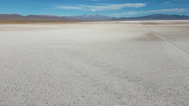 Aerial view of the vast Salinas Grandes salt flats with geometric patterns and distant mountains under a blue sky in Tumbaya, Jujuy, Argentina.