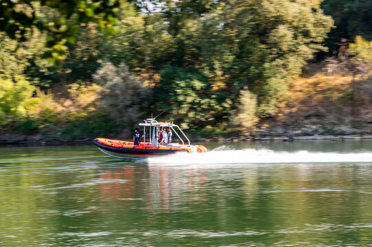 Red rigid inflatable rescue boat speeding down a green river leaving a white wake