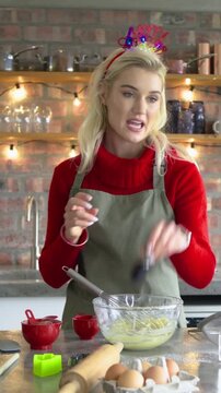 Vertical video: Whisking home baker wearing red sweater, adding vanilla to make batter in kitchen