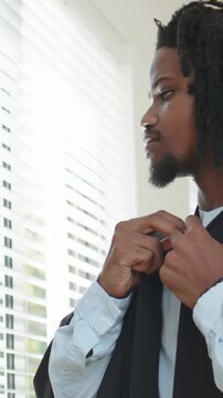 Vertical video: Preparing for event, man fastening robe clasp by blinds, adjusting tie, copy space