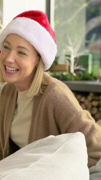 Vertical video: Speaking woman in Santa hat responding to off-camera question on couch, tree